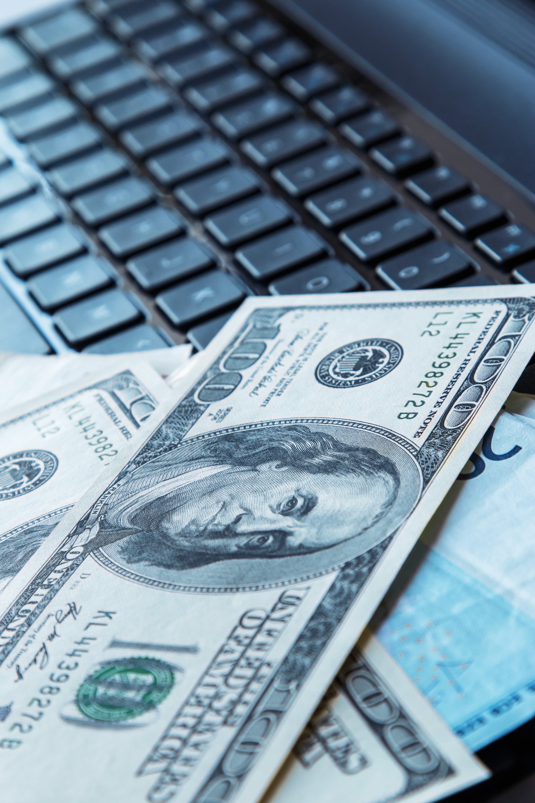 A stack of dollar bills on top of a laptop keyboard.