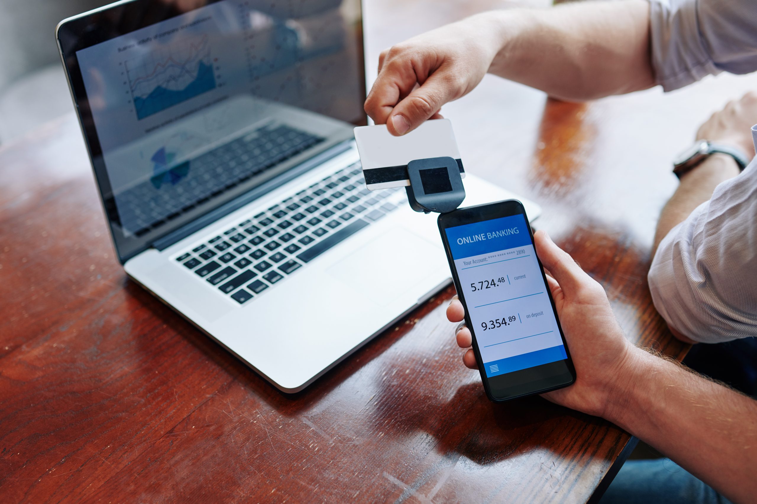 A man is holding a credit card in front of a laptop.