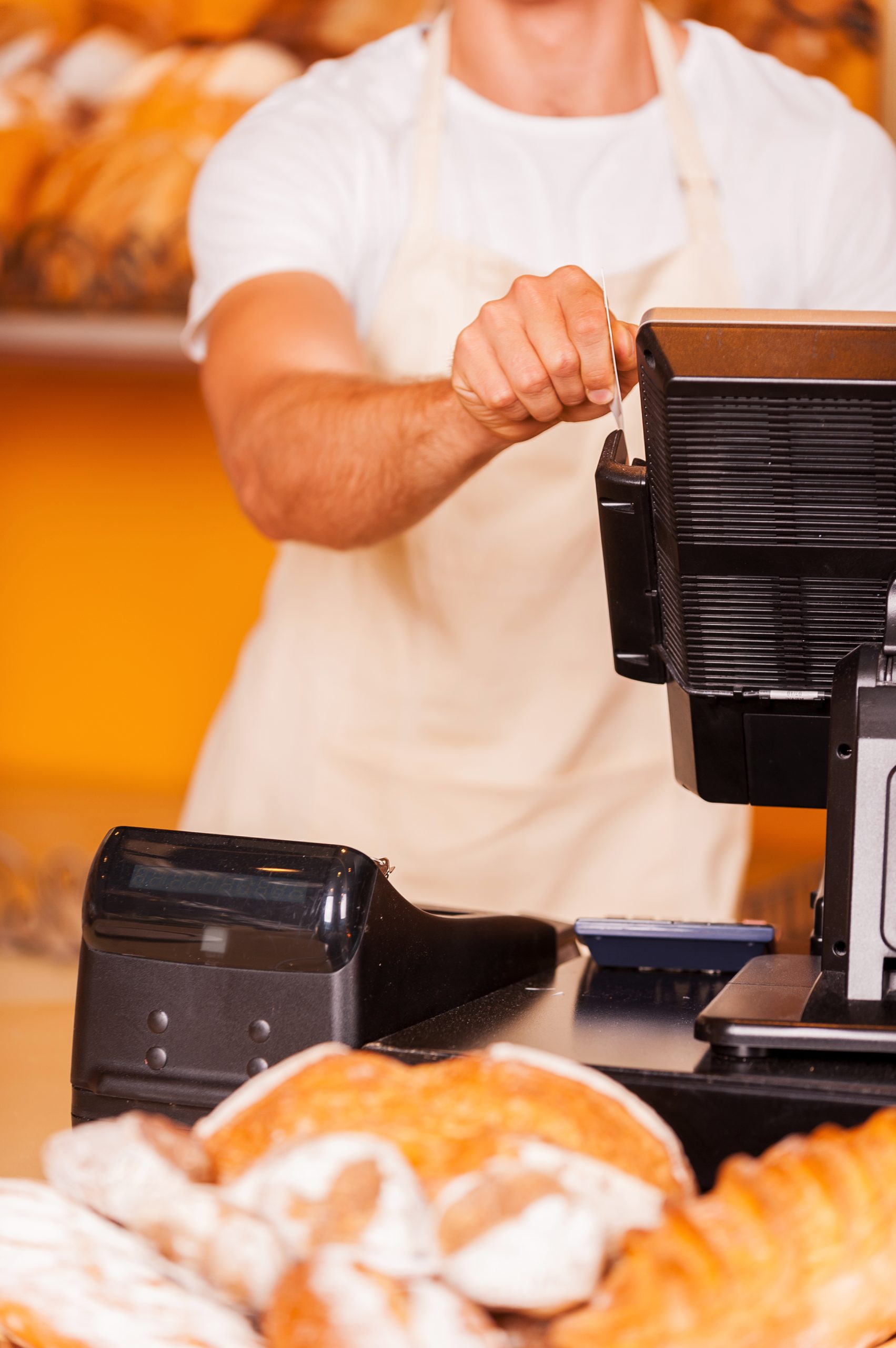 A man is using a cash register in a bakery.