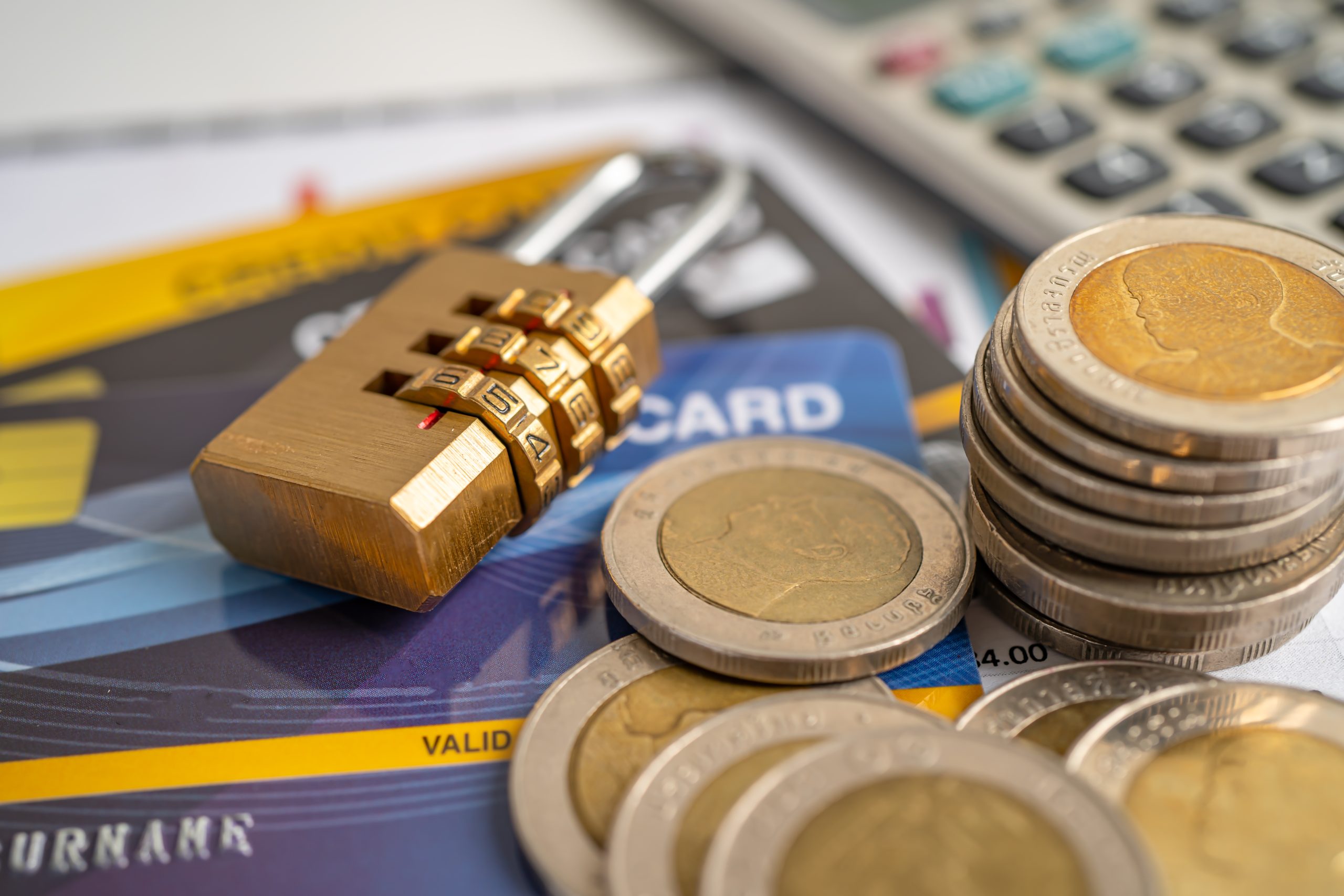 A padlock, coins and a calculator on top of a desk.