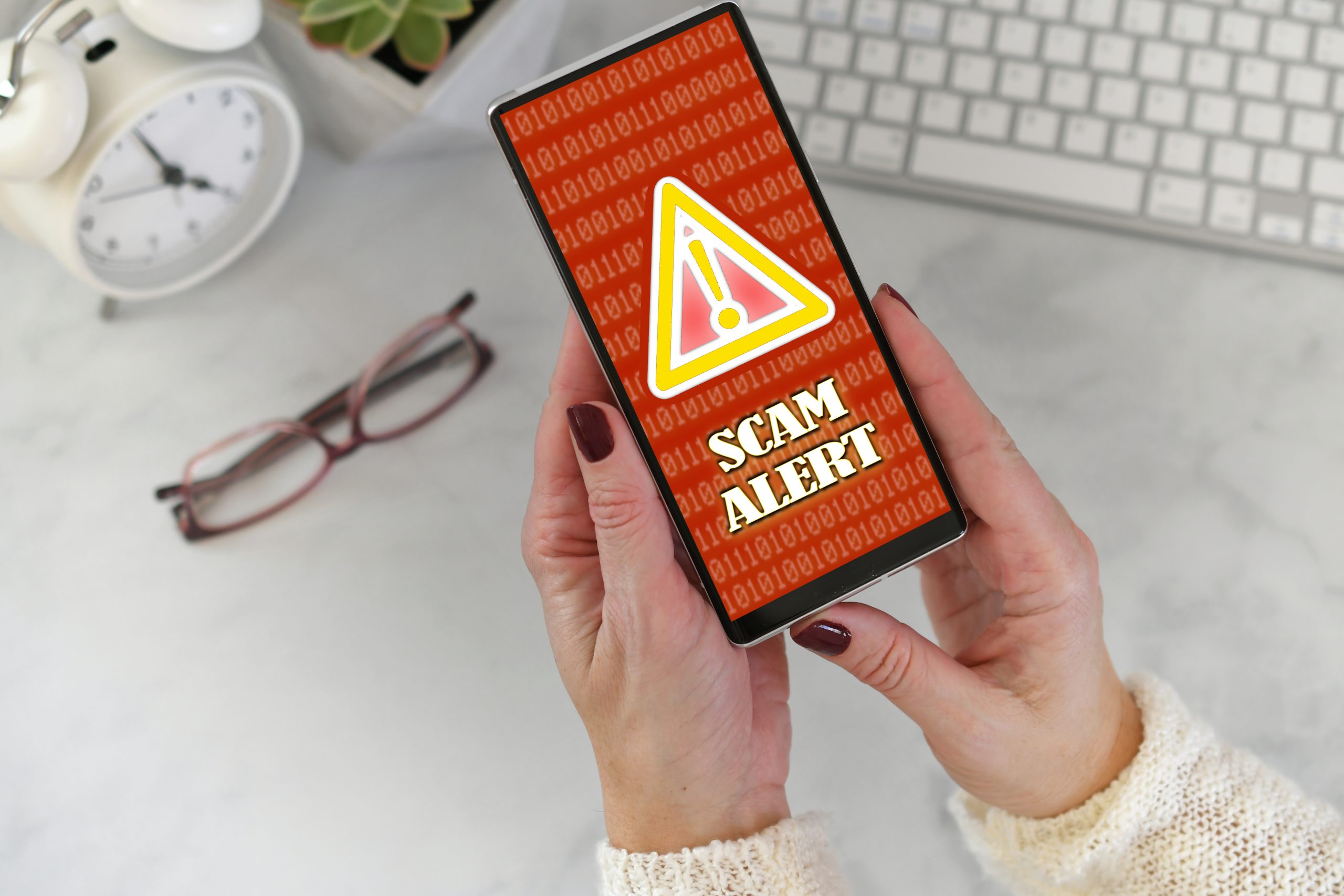 A woman holding up a smartphone with the word scam alert on it.