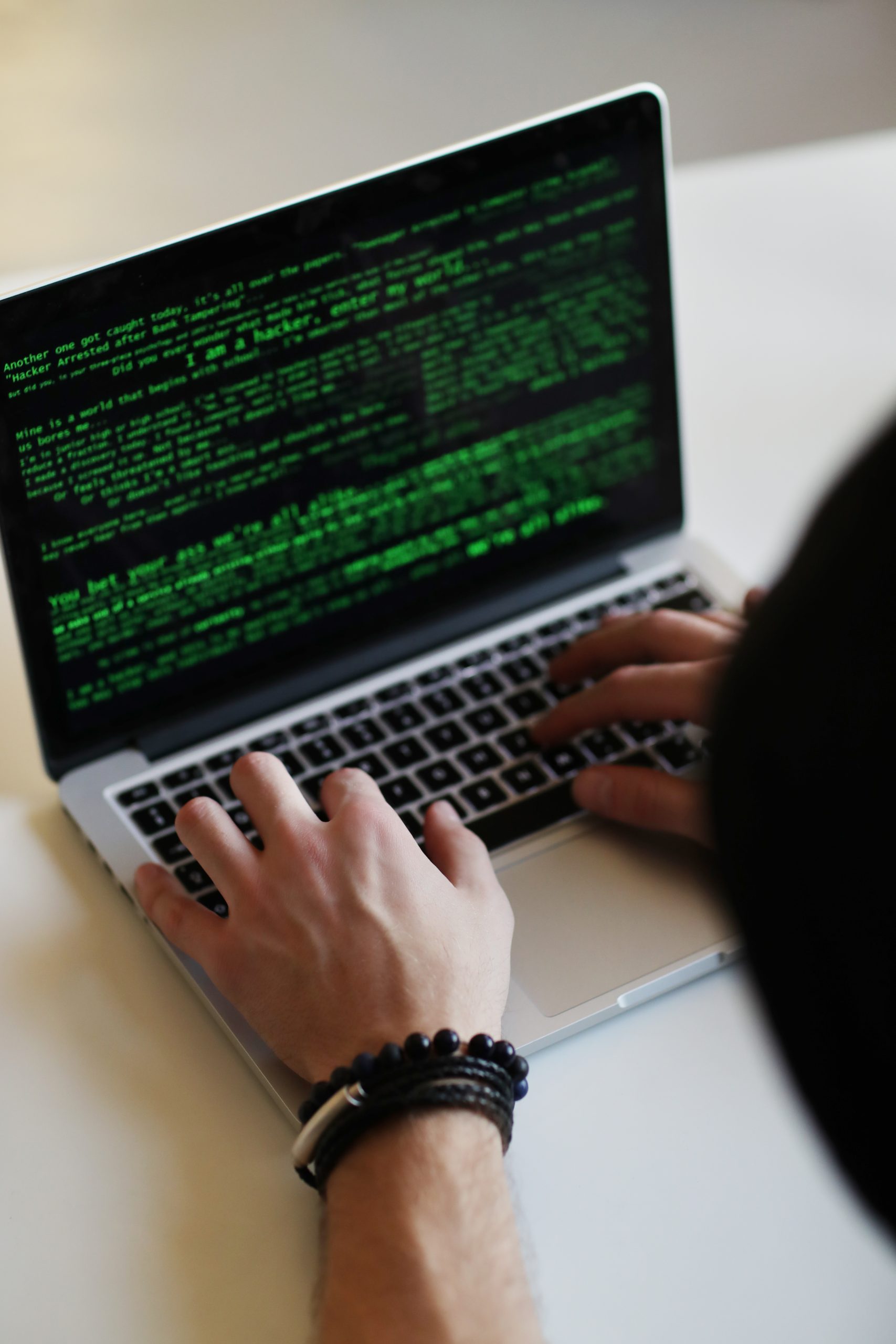 A person typing on a laptop with green code on it.