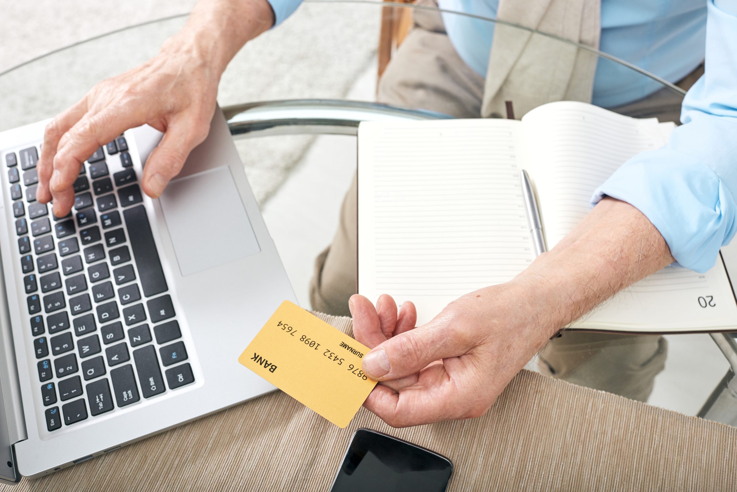 A man holding a credit card while using a laptop.