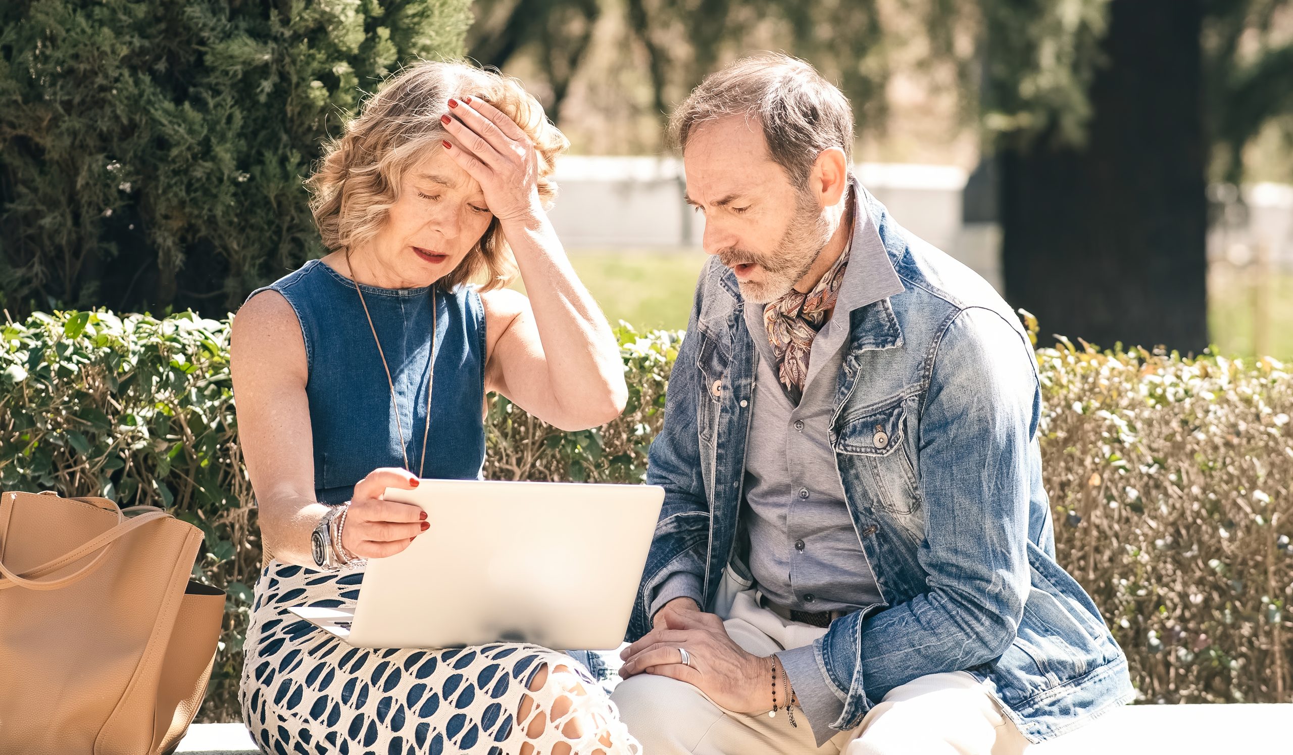 A man and woman sitting on a bench looking at a laptop.
