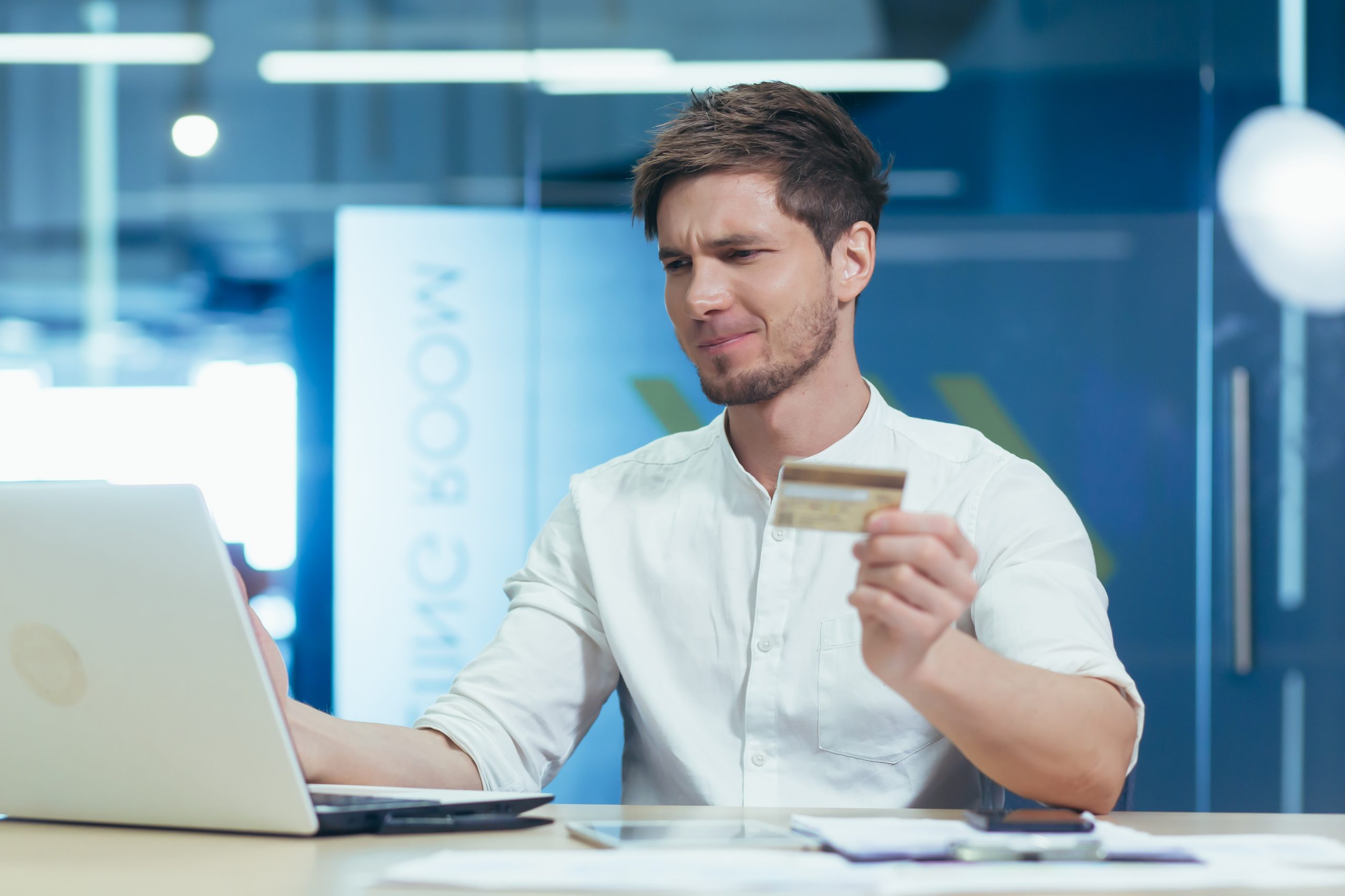 A man holding a credit card in front of a laptop.