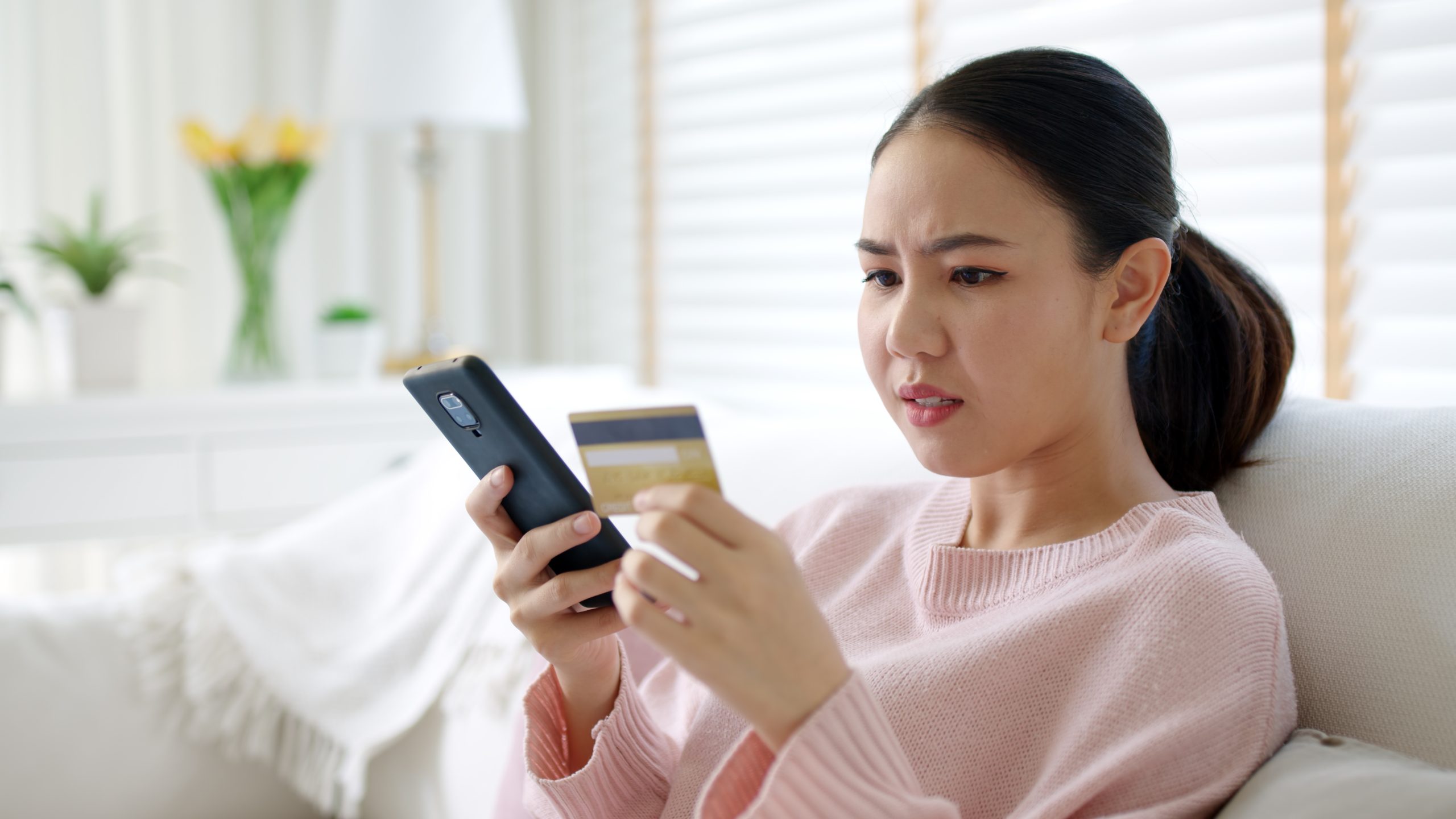 A woman is sitting on a couch with a credit card in her hand.